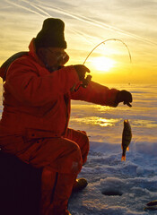 An ice angler with a perch at sunset 