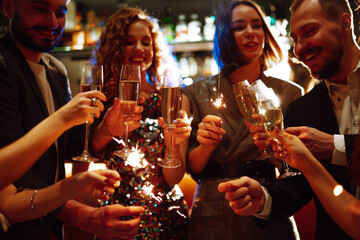 Sparkling sparklers in the hands of friends.Group of people holding sparklers at party. Winter...