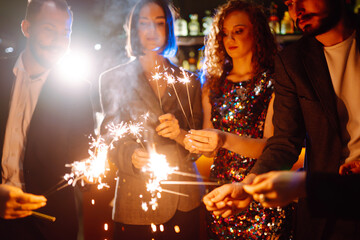 Sparkling sparklers in the hands of friends.Group of people holding sparklers at party. Winter...
