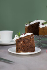 A piece of Christmas cake on plate on grey table with cup of tea and christmas cake on the glass stand.