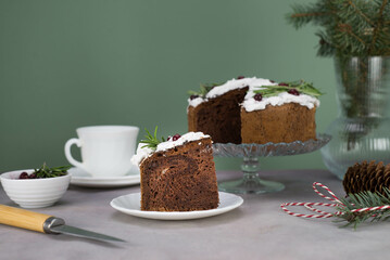 A piece of Christmas cake on plate on grey table with cup of tea and christmas cake on the glass stand.