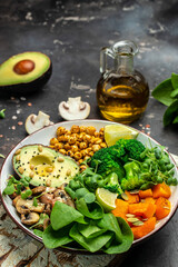 healthy vegan lunch bowl with Avocado, mushrooms, broccoli, spinach, chickpeas, pumpkin on a dark background. vegetables salad. Top view