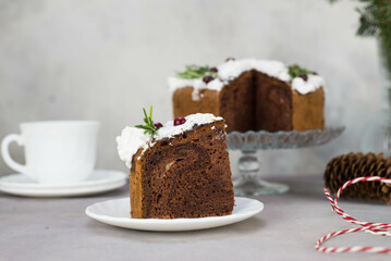 A piece of Christmas cake on plate on grey table with cup of tea and christmas cake on the glass stand.
