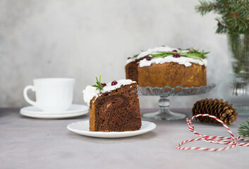 A piece of Christmas cake on plate on grey table with cup of tea and christmas cake on the glass stand.