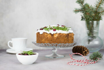 Christmas cake with rosemarry and red berries on a stand on a gray background.