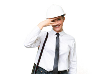 Young architect caucasian woman with helmet and holding blueprints over isolated background covering eyes by hands and smiling