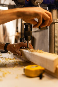 Male hands and vertical wood drilling machine in carpentry workshop