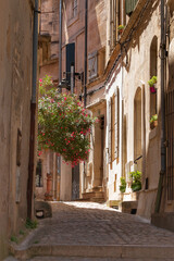 A typical, narrow, picturesque street in the Provence region of France. A street with building facades and colorful flowers in the city of Arles. Summer in the Mediterranean region.