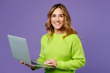 Young fun smiling happy IT woman 30s she wears casual green knitted sweater hold use work on laptop pc computer isolated on plain pastel purple background studio portrait. People lifestyle concept. - obrazy, fototapety, plakaty
