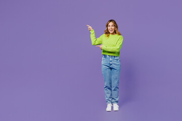 Full body young fun woman 30s she wear casual green knitted sweater point index finger aside indicate on workspace area copy space mock up isolated on plain pastel purple background studio portrait