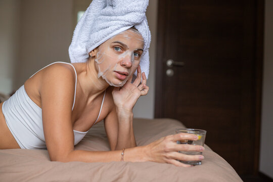 Beauty portrait woman with a towel wrapped around her head lying on the bed with glass of water 