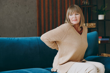 Side view elderly sad woman 50s year old wear casual clothes sits on blue sofa Feels bad suffering...