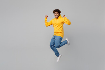 Fototapeta na wymiar Full body successful lucky fun young Indian man 20s he wearing casual yellow hoody jump high do winner gesture clench fist isolated on plain grey background studio portrait. People lifestyle portrait.