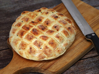 turkish flatbread with black cumin on wooden cutting board with bread knife, round wheat bread for...