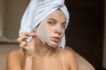 Beauty portrait woman with a towel wrapped around her head taking off sheet mask