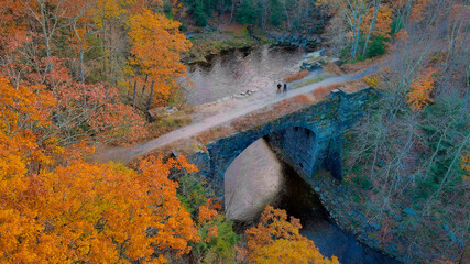 Autumn forest on the riverside, beautiful stone bridge on a background of cliffs. Filming keystone arch bridges trail in Massachusetts