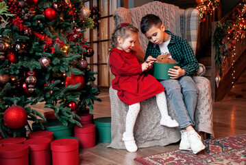 a boy and a girl are sitting with a rabbit, a symbol of the new coming year 2023, next to the Christmas tree