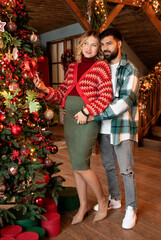 young couple in anticipation of a child stands next to a decorated Christmas tree at home. Christmas concept