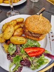 Food on a plate in a Parisian cafe. Burger bun with meat, fried potatoes and salad, tomatoes. Quick lunch in France. A beautifully served plate of food.