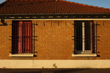 Two old windows with red shutters and grates in front in brick house - one window open, one window closed. Seen at golden hour. Urban concept house (Paris, France) - Powered by Adobe