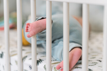 Cute baby feet protrude over the sides of the crib