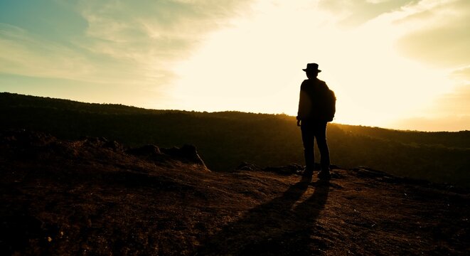 Silhouette shot of a man in hat standing on top of hill and watching the sunrise