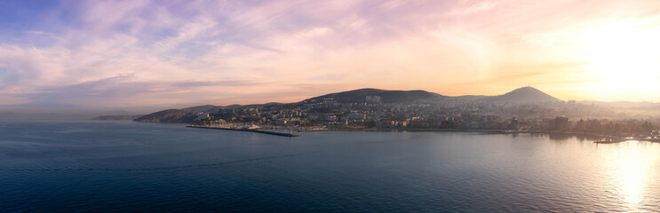 Naklejka na ściany i meble Homes and Buildings in a Touristic Town by the Aegean Sea. Kusadasi, Turkey. Colorful Sunrise Art Render. Panoramic Aerial View from Cruise Ship
