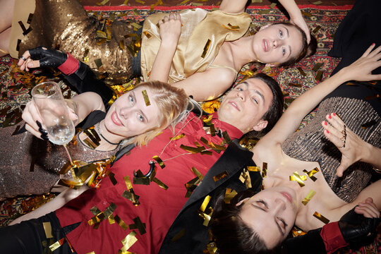 Young man and three women posing on camera lying on rug at New Year party