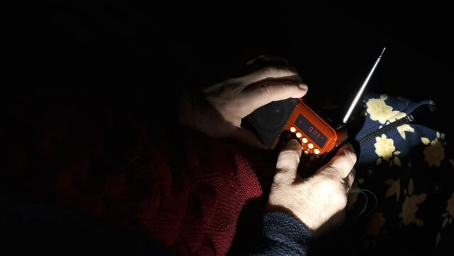 Ukraine, Grandmother hands holds radio in darkness due to blackout during russian terroristic attacks. Senior woman hands with radio receiver listening news.