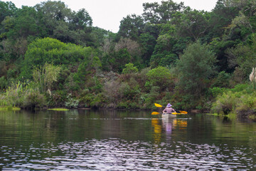 Fototapeta na wymiar Two ladies, one young and one old taking a leisurely paddle on a river in a natural park, with trees and shrubs on the water edge