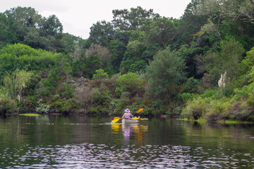 Two ladies, one young and one old taking a leisurely paddle on a river in a natural park, with trees and shrubs on the water edge