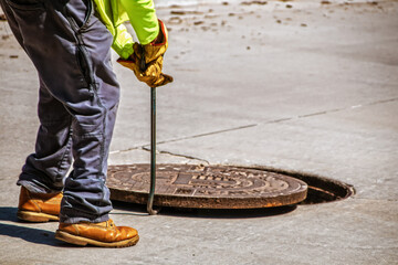Man removing or replacing a heavy manhole cover in paved street with hook - selective focus and...