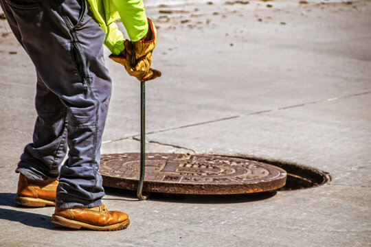 Man removing or replacing a heavy manhole cover in paved street with hook - selective focus and copy space