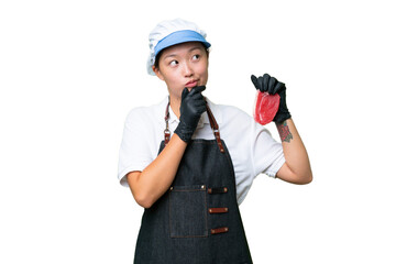 Young caucasian woman wearing an apron and serving fresh cut meat over isolated background and looking up