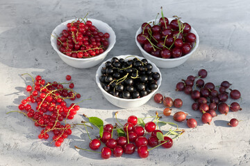 Ripe juicy berries - cherries, black and red currants, gooseberries - on a gray concrete background. Summer harvest concept. Homegrown organic eco food 