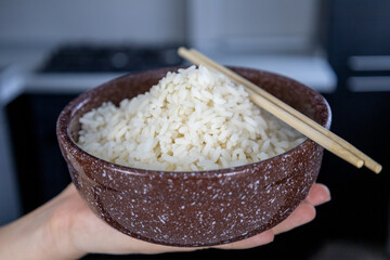 A brown plate with golden rice in the palm of a girl's hand in the kitchen. Asian food concept