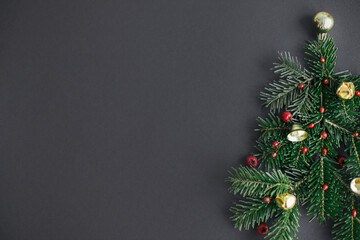 Stylish christmas tree made of fir branches, red berries and gold baubles on black background. Creative christmas idea, winter holidays. Merry Christmas! Modern festive flat lay, space for text