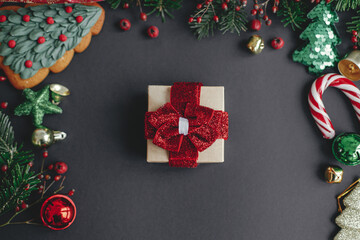 Stylish christmas gift flat lay and branches, red berries, gold ornaments frame on black background. Season's greeting card, winter holidays. Merry Christmas and Happy Holidays!
