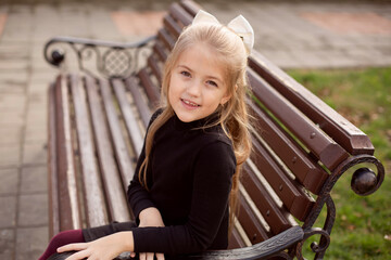 a beautiful blonde girl with long hair in a black dress is sitting on a park bench