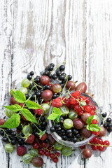Summer fresh berries gooseberry with red and black currant in glass jar on wooden table