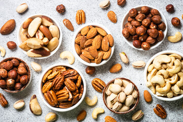Assortment of nuts in bowls. Cashew, hazelnuts, pecan, almonds, brazilian nuts and pistachios. Top view with at Light stone table.