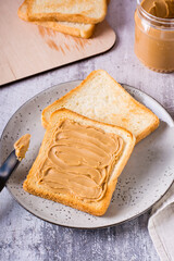 Bread toast with peanut butter on a plate and a jar of butter on the table. Vertical view