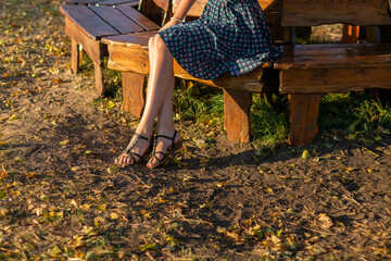 cropped image of slender female legs. Woman sitting on a wooden bench in autumn park
