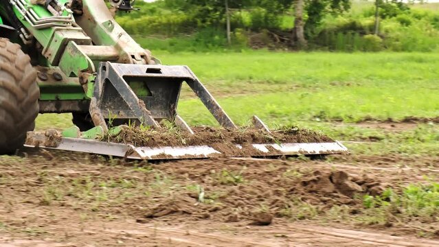 Land work by the territory improvement. Small tractor with a ground leveler for moving soil, turf. A green mini skid steer loader clear the construction site. Machine for agriculture work. Copy space.