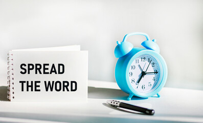 Notepad with text SPREAD WORD on white background with clock
