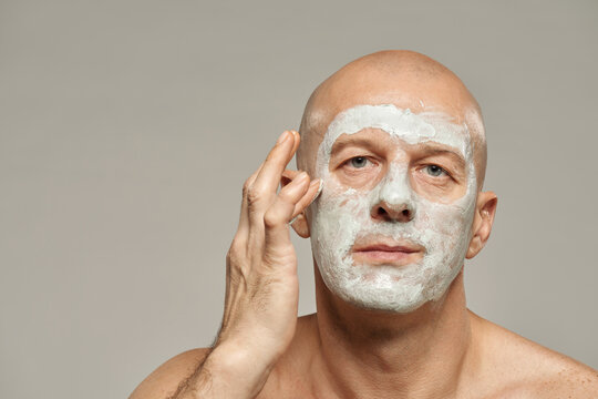 Attractive mature man applying kaolin clay mask on his face horizontal beauty portrait