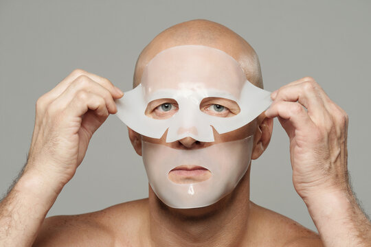 Horizontal portrait of adult man taking off hydrogel collagen mask after using it