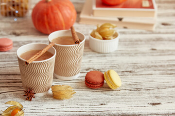 Aesthetics cardboard cups of pumpkin latte and cinnamon sticks among autumn decorations. Seasonal coffee time with macaroons and winter cherry. Cozy atmospheric home.