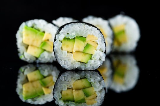 Fresh maki sushi rolls with rice and avocado on a black.