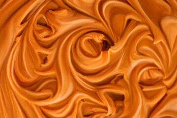 Liquid melted caramel syrup. Background of caramel syrup, paste. Curl, wave of caramel. Texture, Close up, top view.